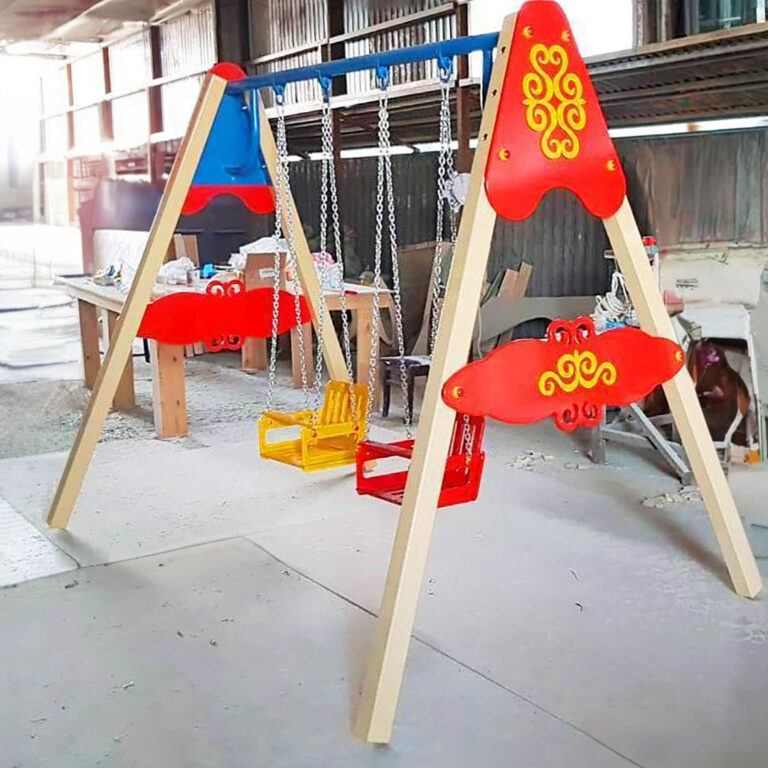 Деревянная яркая детская качеля на двоих с национальными казахскими орнаментами в производственном цеху.